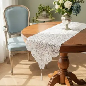 Weißer Tischläufer aus Spitze mit Blumenmuster und Quaste auf einem runden Holztisch mit Vase
