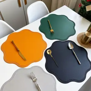 Wellenförmige Platzsets aus Kunstleder in Orange, Grün, Dunkelblau und Grau auf einem weißen Tisch mit Besteck
