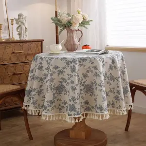 Runde Tischdecke mit blauem Blumenmuster auf hellem Grund und Quasten am Rand auf rundem Tisch