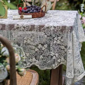Cremefarbene Tischdecke mit Blütenstickerei auf einem gedeckten Gartentisch