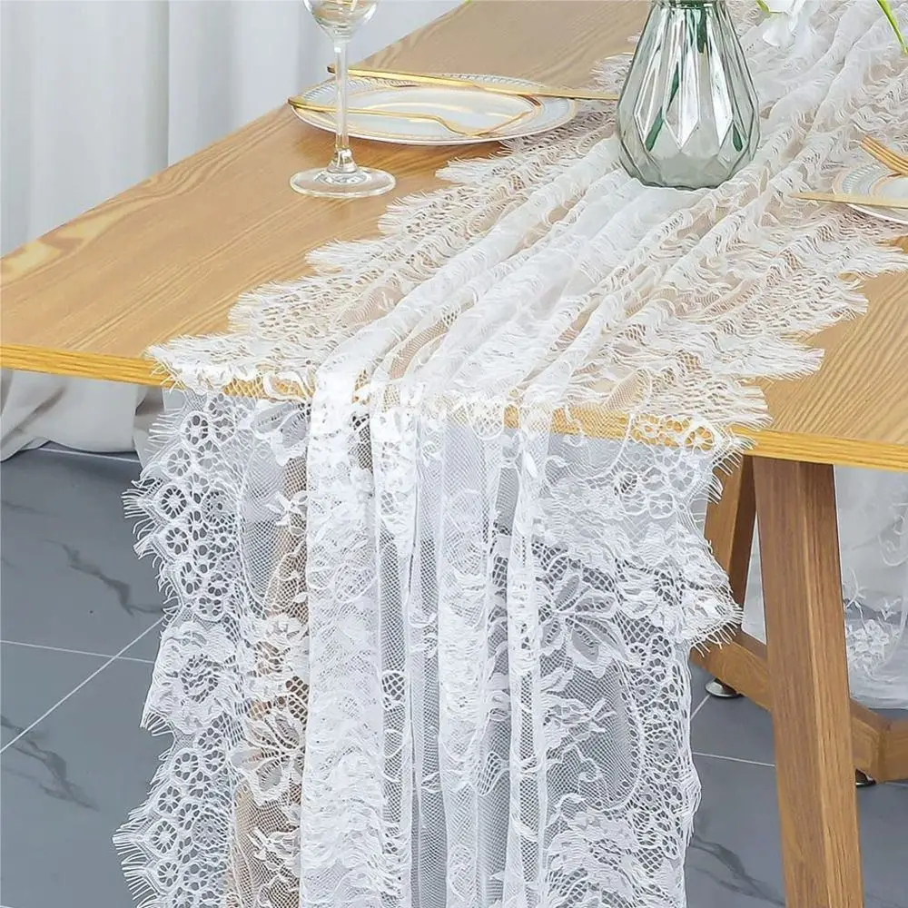 Weißer Tischläufer in Spitzenoptik mit Blumenmuster und gewelltem Rand auf einem Holztisch mit Vase