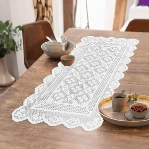 Weißer gehäkelt wirkender Tischläufer mit Zackenrand auf einem Holztisch