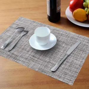 Graues, meliert strukturiertes Tischset auf Holztisch mit Besteck und Tasse