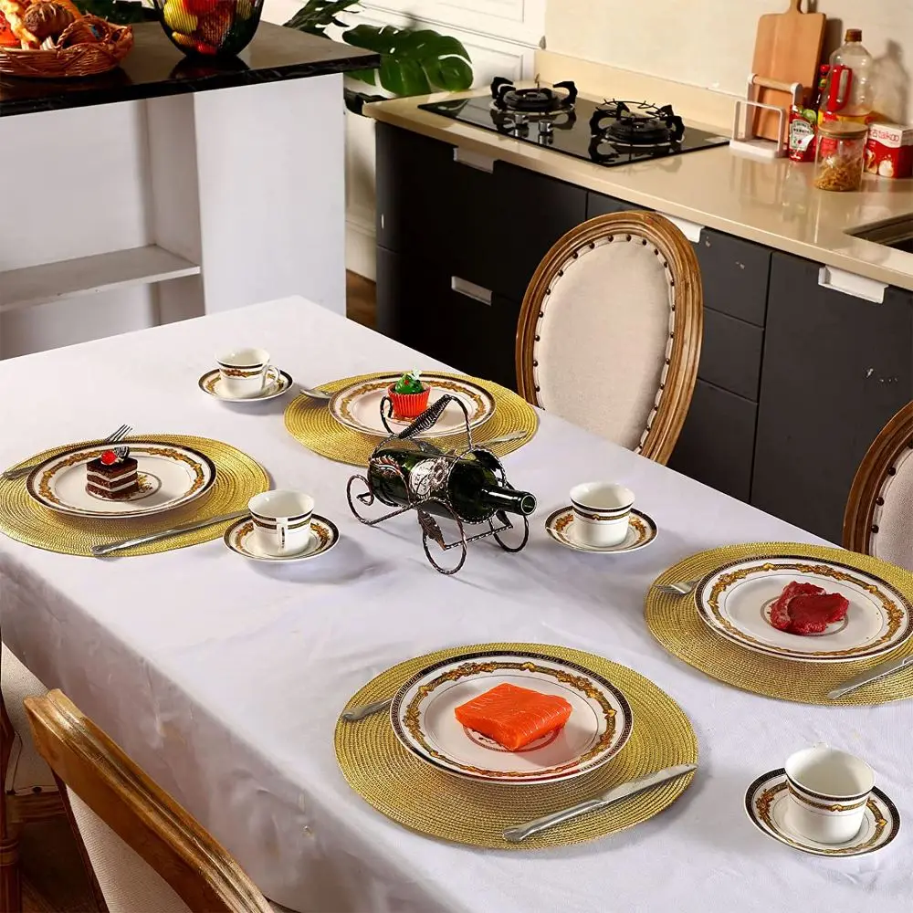 Runde goldfarbene geflochtene Tischsets mit Tellern und Tassen auf einem weißen Tischtuch